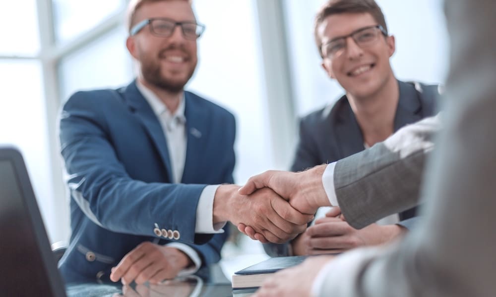 Review Your Business Insurance Coverage - Business Men at a table shaking hands.