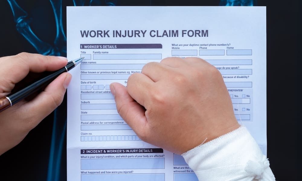 filling up a work injury claim form with a wrapped hand on top of an X-ray film medical and insurance concept