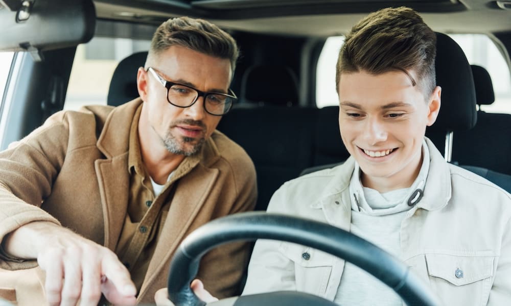 handsome father pointing on something while teaching smiling teen son driving car